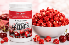 Gold Medal Signature Blends® Red Cherry Premium Flavor & Color Concentrate jar displayed beside a bowl of glossy, bright red cherry-coated popcorn, illustrating the finished product created with the flavor concentrate.